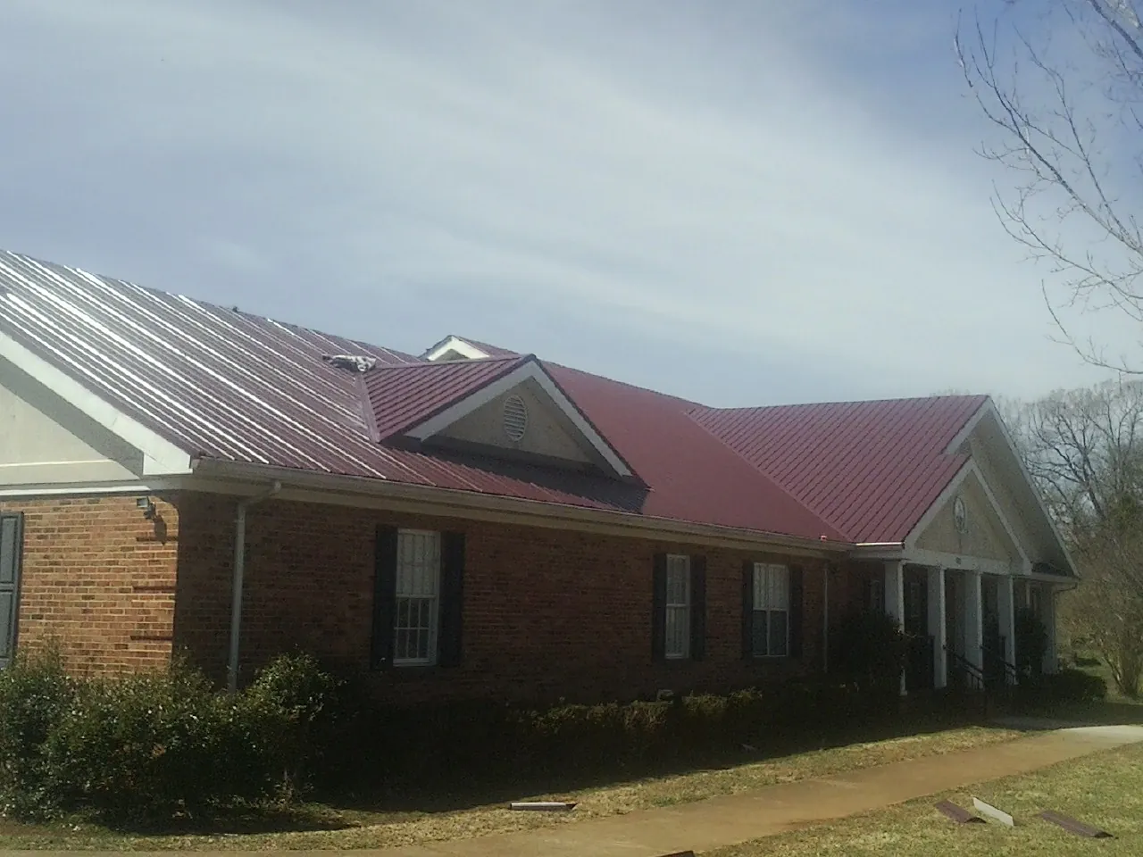 Red metal roof with gabled entries on a long brick building, from a Hail Damage Roof Repair job in Williamston